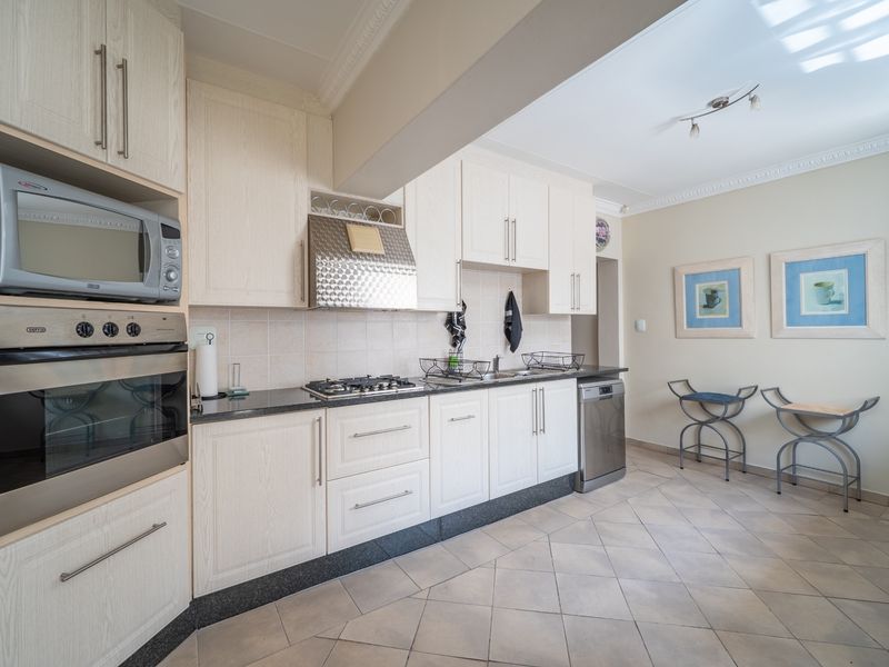 A functional kitchen featuring light-toned cabinetry, granite countertops, built-in oven, microwave, and gas hob, complemented by tiled flooring and coved ceiling details.