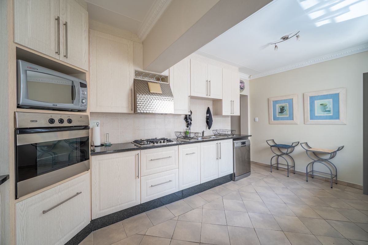A functional kitchen featuring light-toned cabinetry, granite countertops, built-in oven, microwave, and gas hob, complemented by tiled flooring and coved ceiling details.