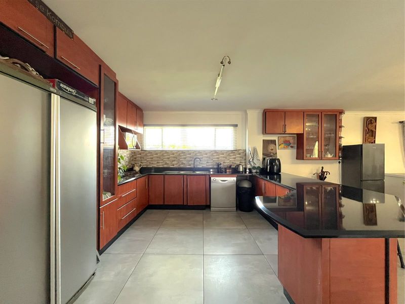 Spacious kitchen featuring warm-toned wooden cabinetry, sleek black granite countertops, large format floor tiles, and a functional layout with ample storage.