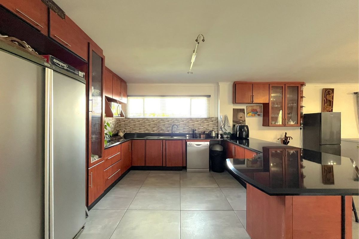 Spacious kitchen featuring warm-toned wooden cabinetry, sleek black granite countertops, large format floor tiles, and a functional layout with ample storage.