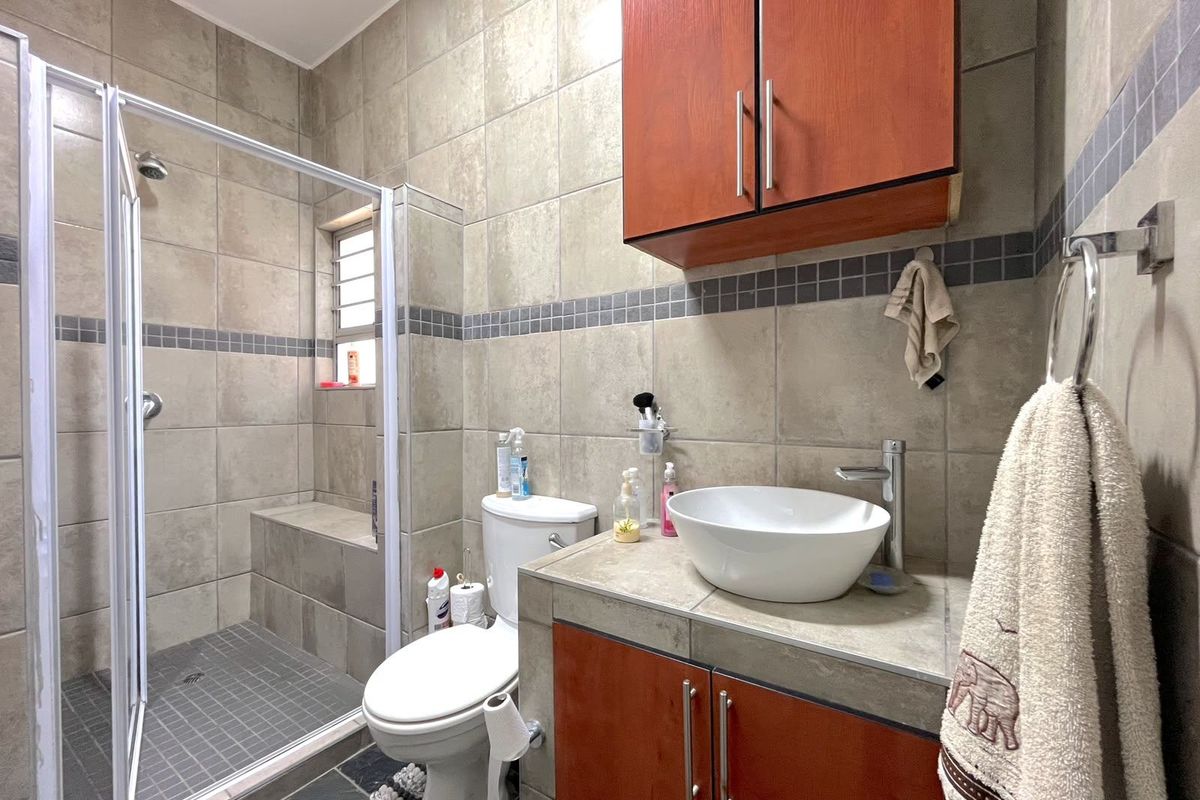 A functional bathroom featuring a tiled shower enclosure, a vessel sink with a vanity cabinet, and neutral wall tiling.
