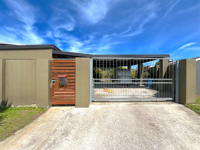 Front exterior view featuring a concrete driveway, sliding metal gate, timber pedestrian gate, and a covered carport area.