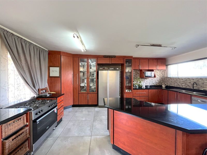 Spacious kitchen featuring cherry-wood cabinetry, granite countertops, a central island, gas stove, and tiled flooring, offering ample storage and workspace.