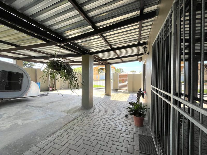 A covered outdoor patio area featuring paved flooring, concrete support pillars, and a corrugated metal roof, providing a functional sheltered space.