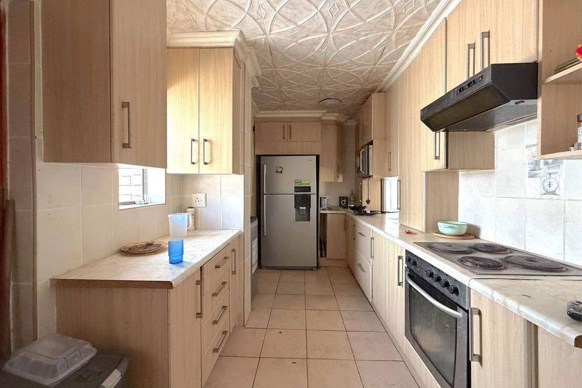 A functional galley-style kitchen featuring light wood-tone cabinetry, tiled flooring, and a built-in oven with extractor fan.