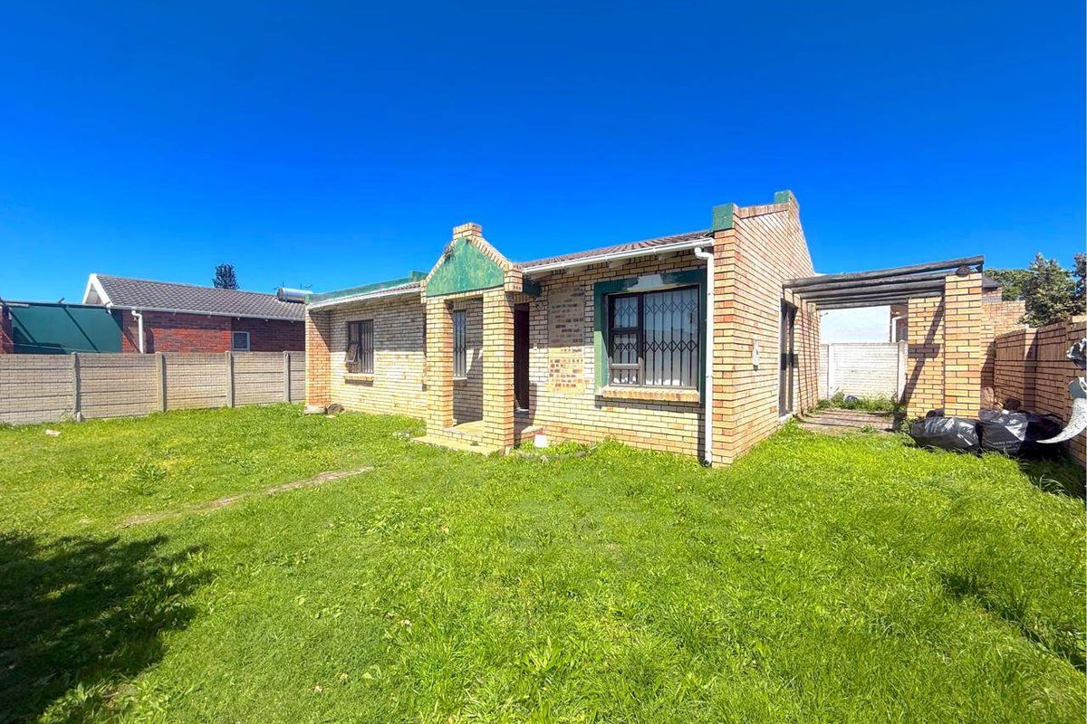 Rear view of a face brick house featuring a small pergola, security bars on windows, and a large, unmaintained garden area.