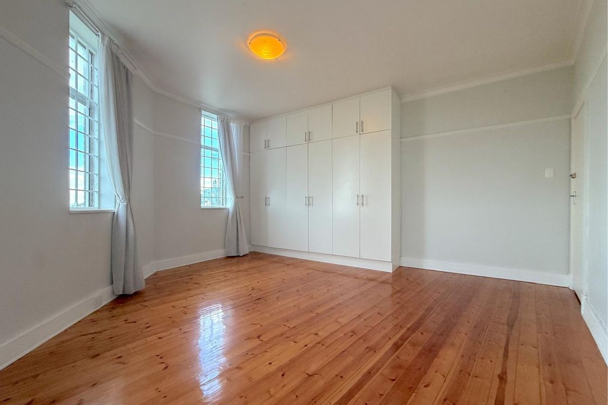A bright and spacious bedroom featuring polished timber flooring, classic picture rails, coved cornicing, and extensive built-in storage cupboards.