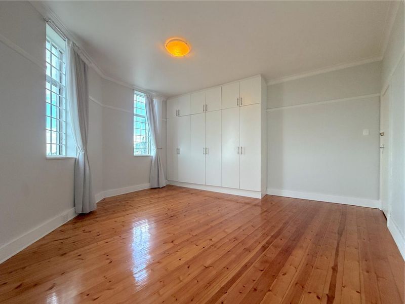 A bright and spacious bedroom featuring polished timber flooring, classic picture rails, coved cornicing, and extensive built-in storage cupboards.