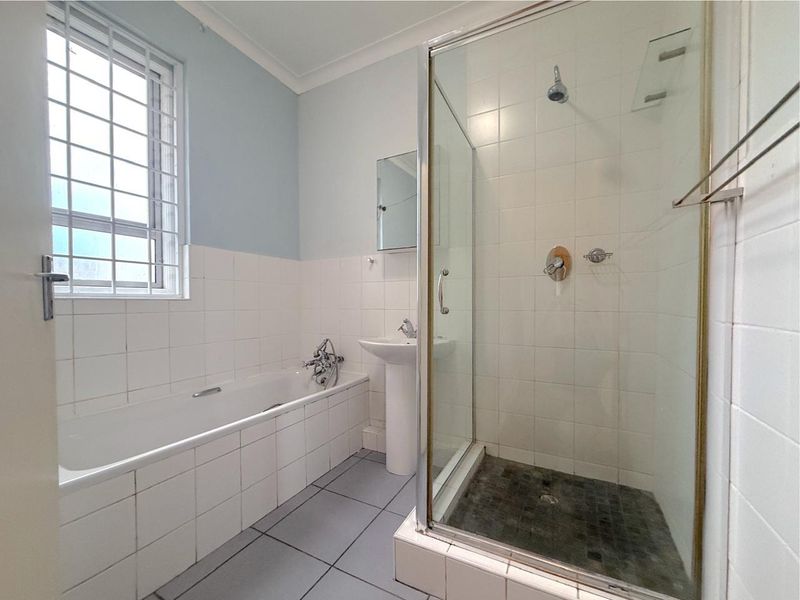 A functional bathroom featuring a built-in bathtub, a separate glass-enclosed shower, and a pedestal sink with tiled finishes throughout.
