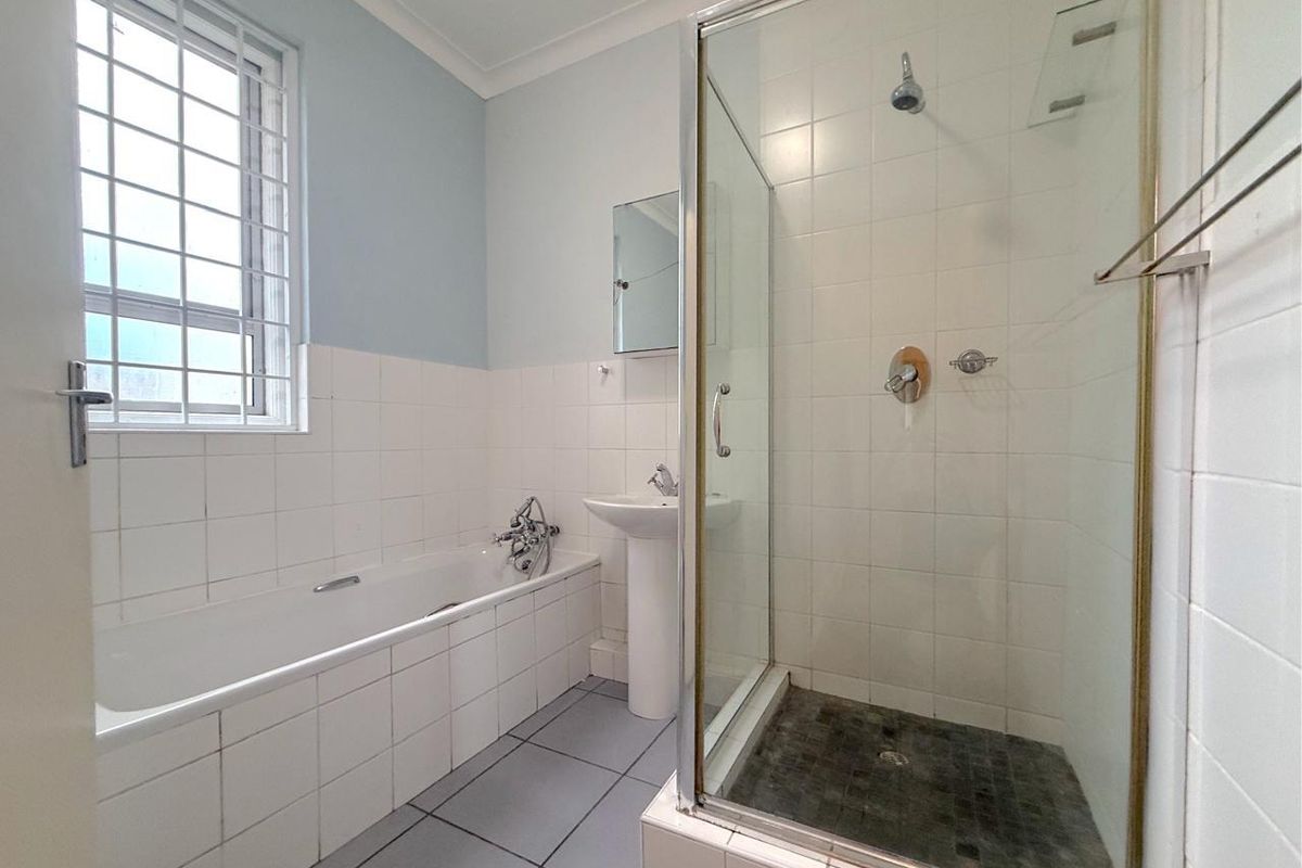 A functional bathroom featuring a built-in bathtub, a separate glass-enclosed shower, and a pedestal sink with tiled finishes throughout.