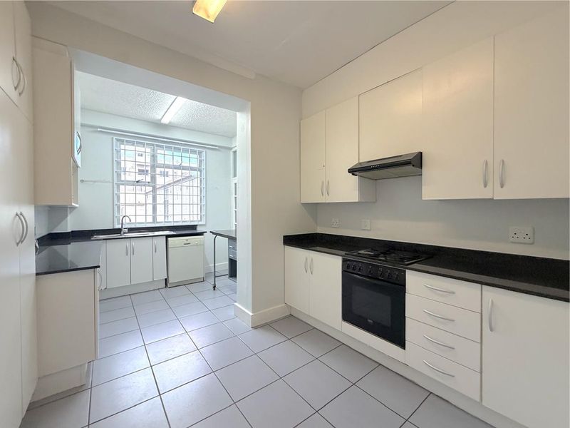 A clean, functional kitchen featuring white cabinetry, black granite countertops, built-in oven, gas hob, and tiled flooring with a separate scullery area.
