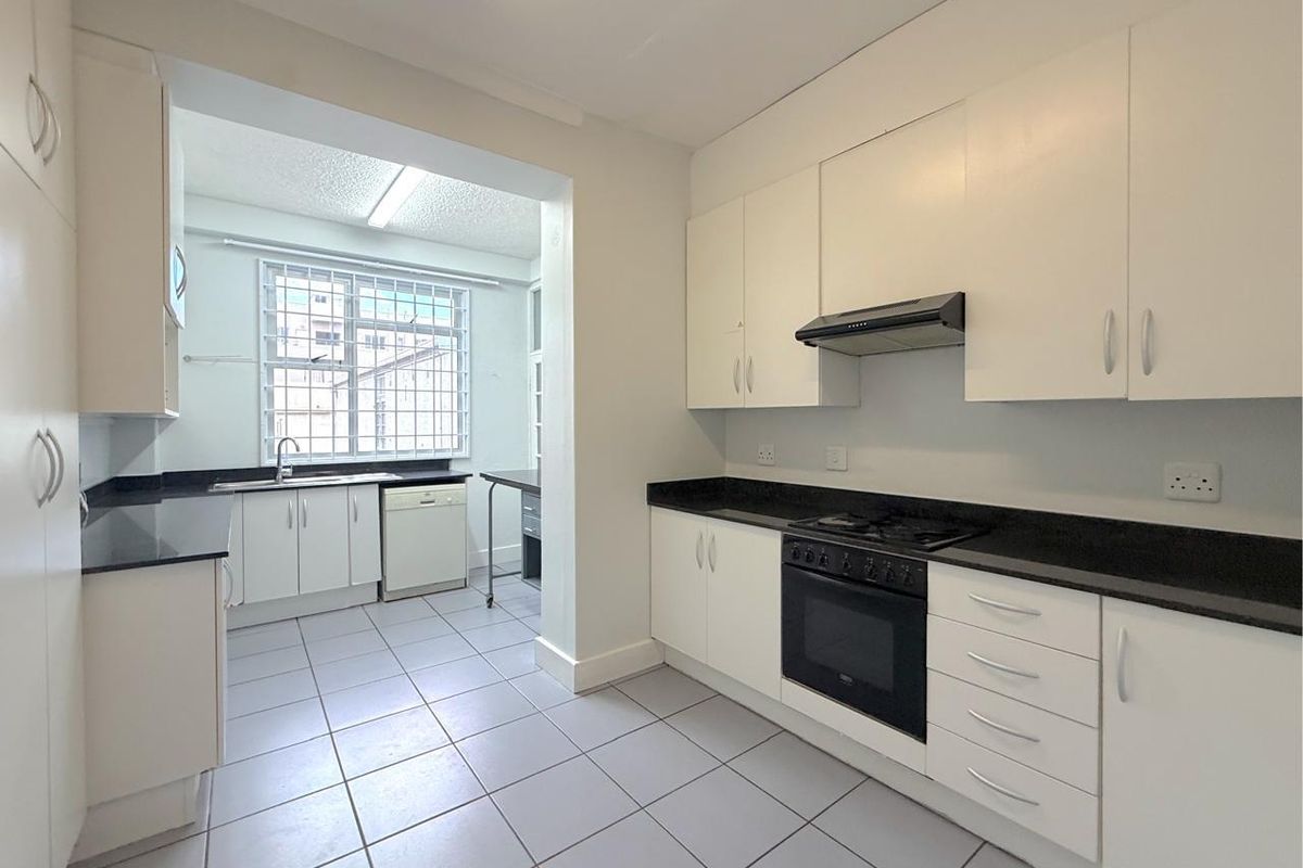 A clean, functional kitchen featuring white cabinetry, black granite countertops, built-in oven, gas hob, and tiled flooring with a separate scullery area.