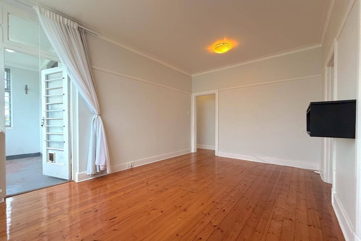 A bright and spacious living room featuring polished hardwood flooring, classic picture rails, and direct access to an adjoining balcony area.