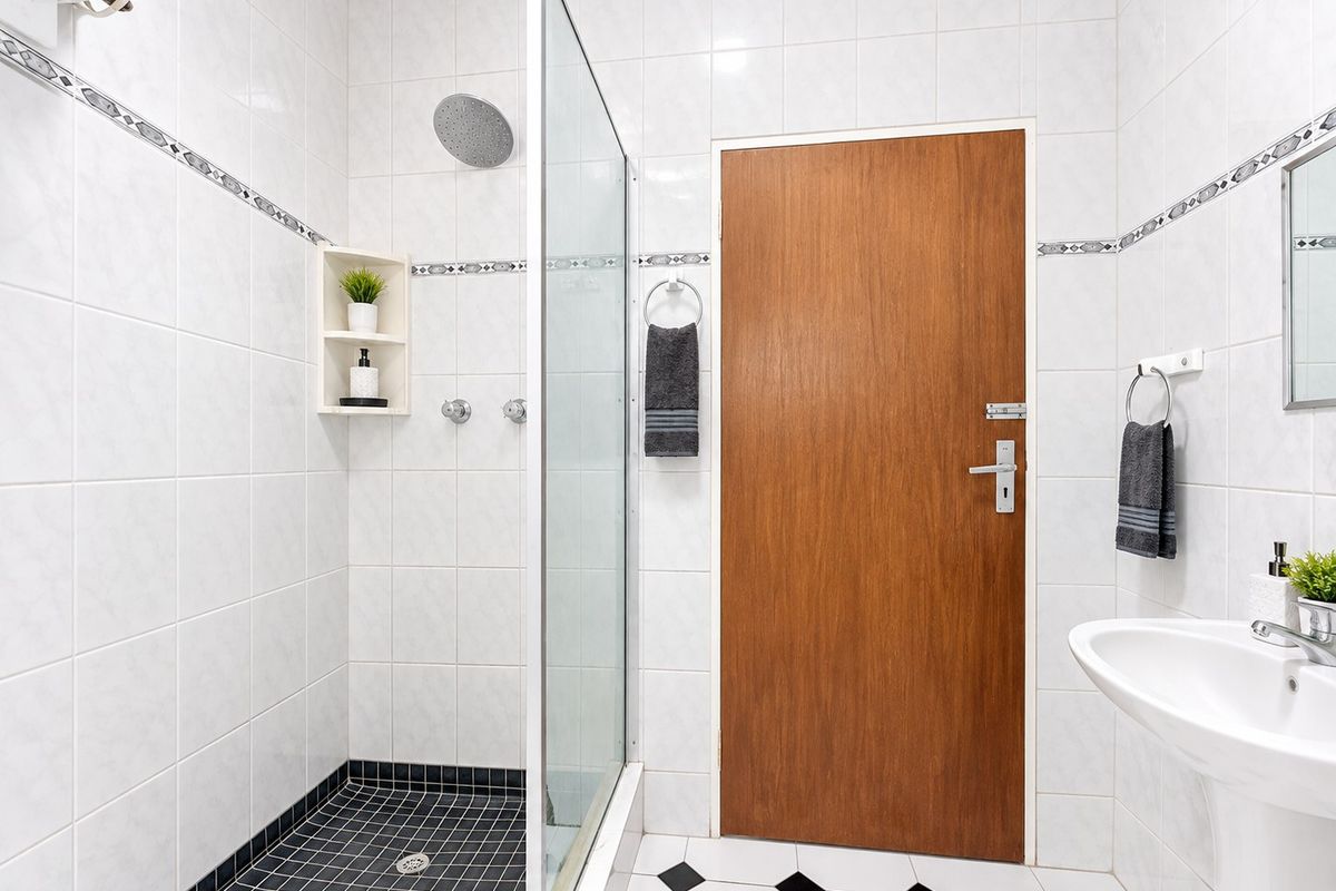 A clean, well-maintained bathroom featuring a walk-in shower with a glass screen, rain shower head, and a classic pedestal sink with tiled finishes.