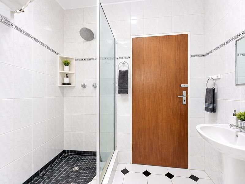 A clean, well-maintained bathroom featuring a walk-in shower with a glass screen, rain shower head, and a classic pedestal sink with tiled finishes.