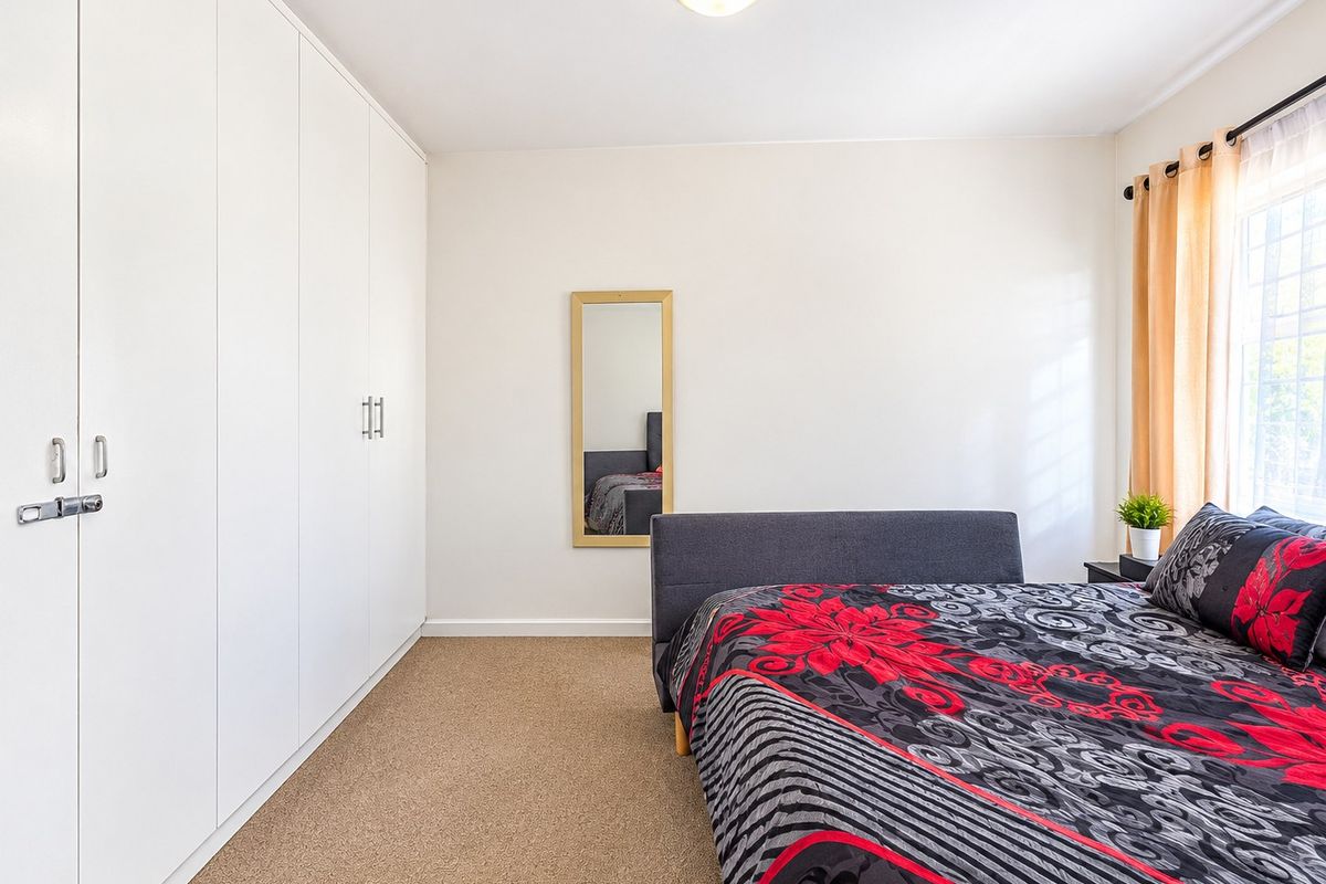 A well-maintained bedroom featuring neutral walls, carpeted flooring, and extensive floor-to-ceiling built-in cupboards for ample storage.