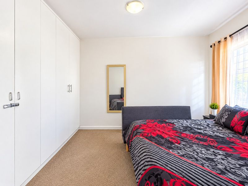 A well-maintained bedroom featuring neutral walls, carpeted flooring, and extensive floor-to-ceiling built-in cupboards for ample storage.
