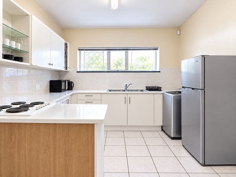A functional kitchen featuring white cabinetry, tiled flooring, a double bowl sink, and an electric hob with a tiled splashback.