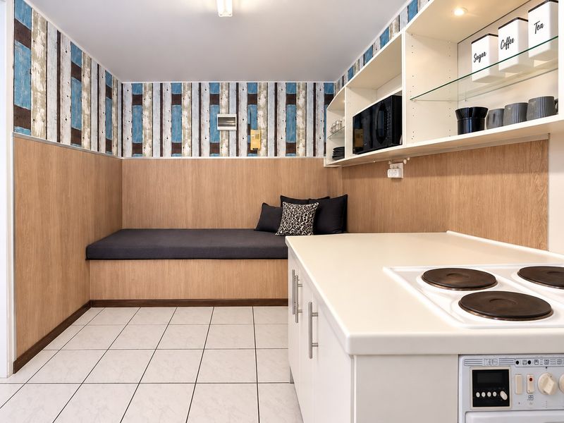 A compact kitchen area featuring built-in bench seating, an electric cooktop, integrated oven, and ample built-in shelving with a modern tiled floor.