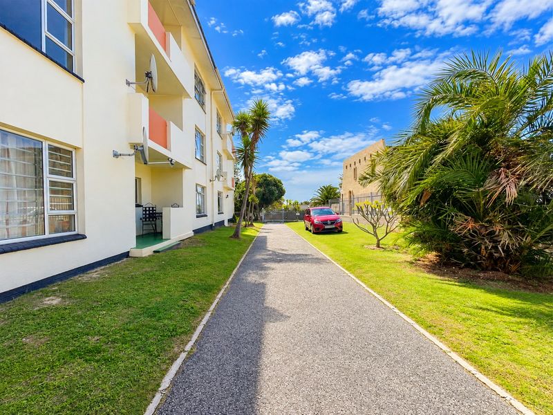 Exterior view of an apartment building featuring a paved walkway, landscaped lawn, and private balconies.