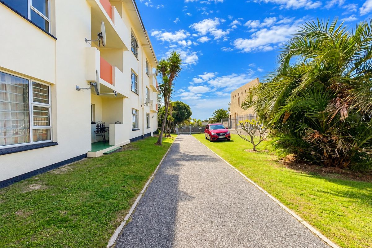 Exterior view of an apartment building featuring a paved walkway, landscaped lawn, and private balconies.