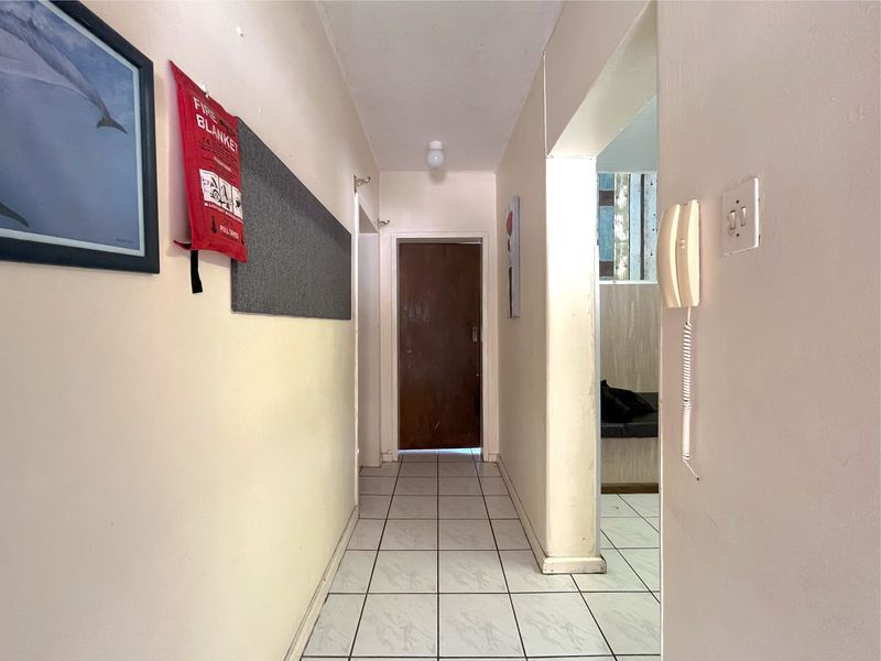 A functional hallway featuring tiled flooring, an intercom system, and access to adjacent rooms, showing signs of wear and requiring cosmetic updates.