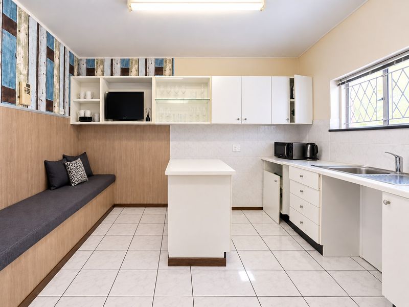 A functional kitchen featuring white cabinetry, a central island, tiled backsplash, and integrated bench seating with a neutral tiled floor.