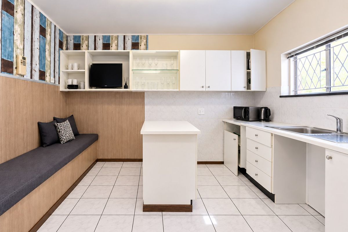 A functional kitchen featuring white cabinetry, a central island, tiled backsplash, and integrated bench seating with a neutral tiled floor.