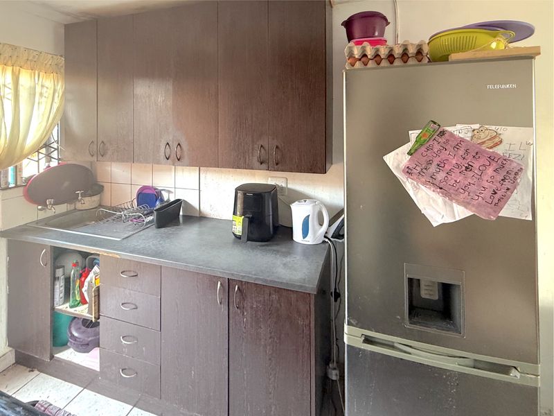 A compact kitchen featuring dark wood-look cabinetry, a laminate countertop, and a stainless steel sink with a tiled backsplash.