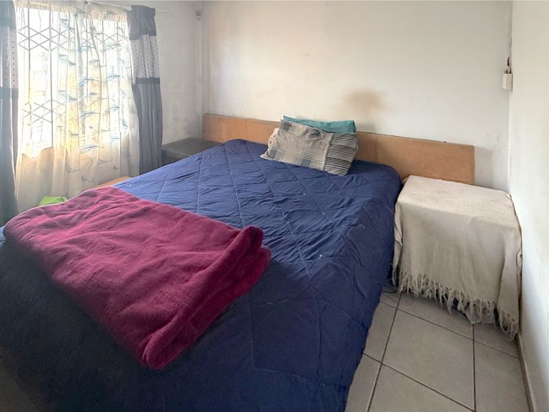 A bedroom featuring tiled flooring and a built-in headboard, currently showing signs of wear on the wall surfaces.