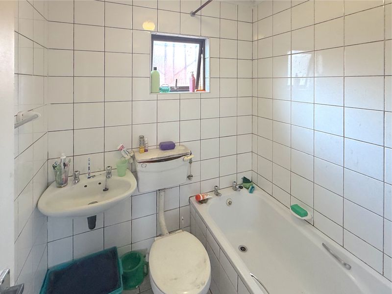 A functional bathroom featuring a bathtub, wall-mounted basin, and toilet, finished with white wall tiles throughout.