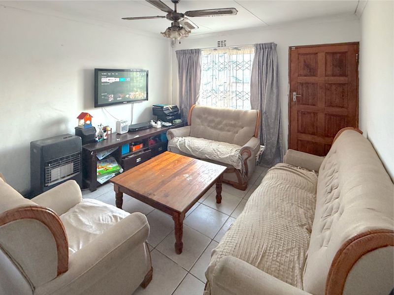 A living room featuring tiled flooring, a ceiling fan, and a timber entrance door, providing a functional space for relaxation.