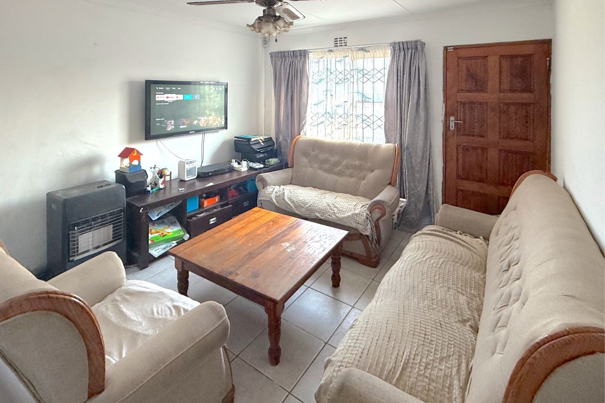 A living room featuring tiled flooring, a ceiling fan, and a timber entrance door, providing a functional space for relaxation.
