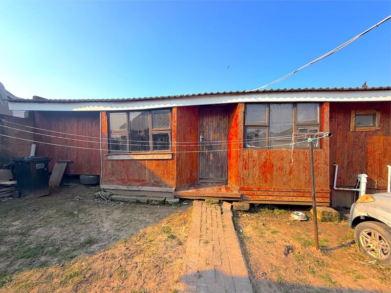Rear view of a timber-clad house featuring a brick walkway and metal roofing, showing signs of significant exterior wear and weathering.
