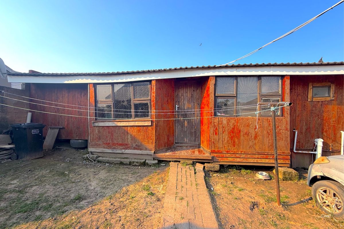 Rear view of a timber-clad house featuring a brick walkway and metal roofing, showing signs of significant exterior wear and weathering.