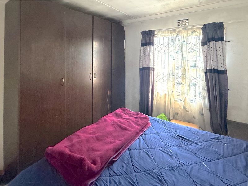 A bedroom featuring built-in cupboards and a window with security gate, requiring cosmetic updates to the ceiling and walls.