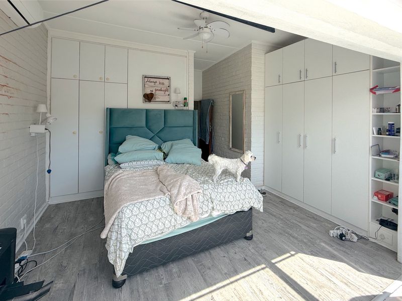 Spacious bedroom featuring extensive built-in cupboard storage, exposed brick feature walls, ceiling fan, and modern laminate flooring.