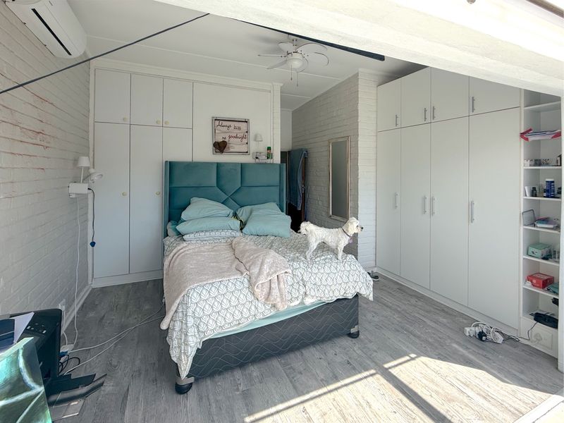 Spacious bedroom featuring extensive built-in cabinetry, laminate flooring, a ceiling fan, and a wall-mounted air conditioning unit.