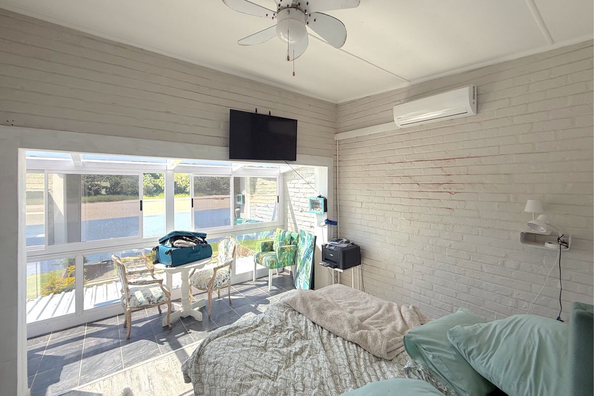 A bedroom featuring painted brick walls, a ceiling fan, split-system air conditioning, and large windows offering natural light and views.