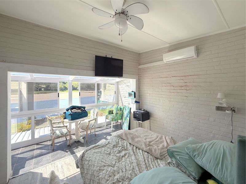 A bedroom featuring painted brick walls, a ceiling fan, split-system air conditioning, and large windows offering natural light and views.