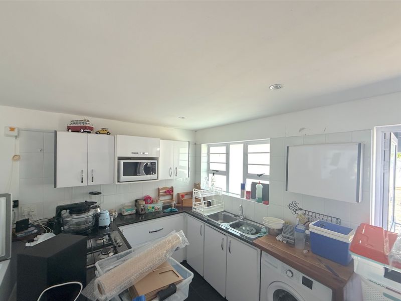 Functional kitchen featuring white cabinetry, granite countertops, a gas hob, built-in microwave, and a double basin sink with tiled backsplash.