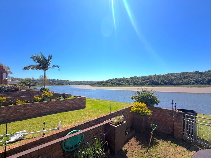 A scenic view of the river and natural landscape from the property's rear garden area, featuring brick retaining walls and lawn.