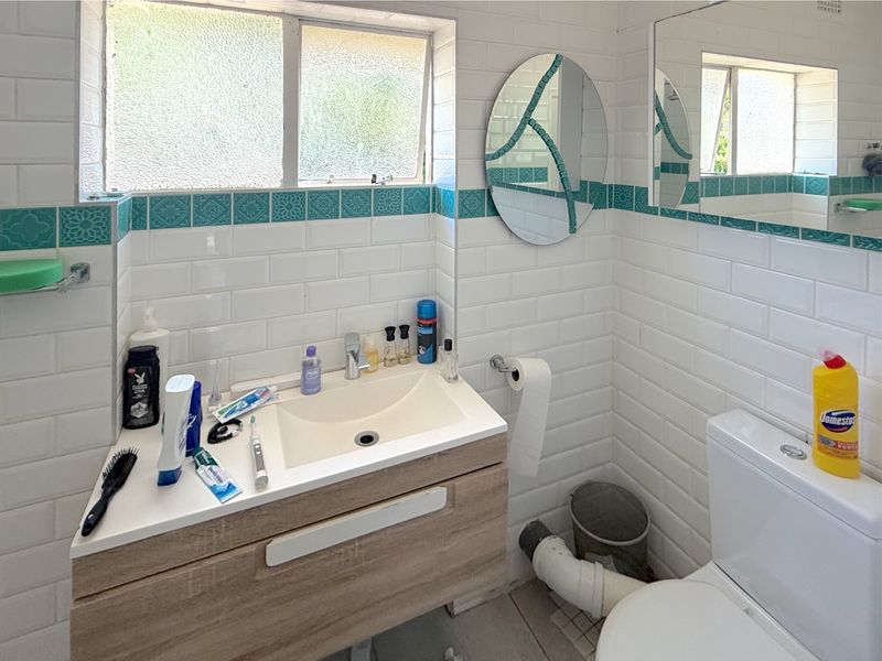 A functional bathroom featuring a modern vanity, subway wall tiling with decorative accents, and a toilet with visible plumbing.