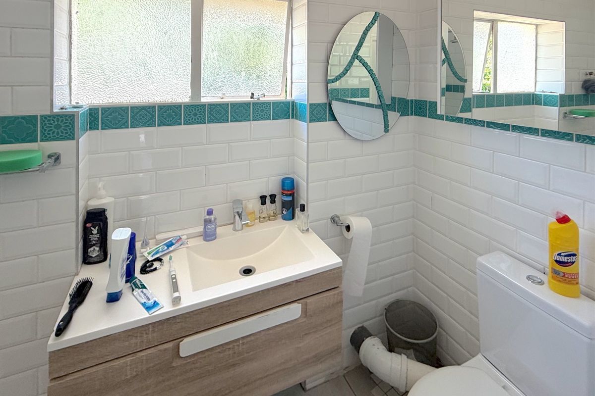 A functional bathroom featuring a modern vanity, subway wall tiling with decorative accents, and a toilet with visible plumbing.