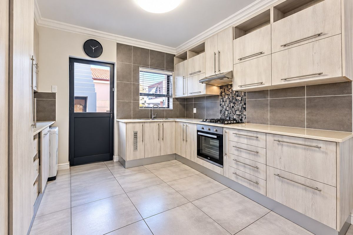 Modern kitchen featuring light wood-grain cabinetry, stone countertops, built-in oven, gas hob, extractor fan, and neutral tiled flooring with a tiled backsplash.