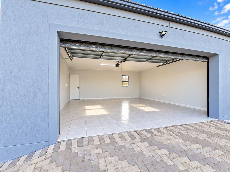 A clean, spacious double garage featuring tiled flooring, a sectional door, and direct access to the interior, set against a paved driveway.