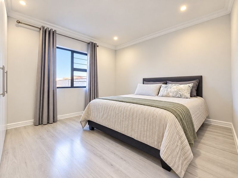 A well-maintained bedroom featuring light-toned laminate flooring, recessed downlighting, and a built-in wardrobe.