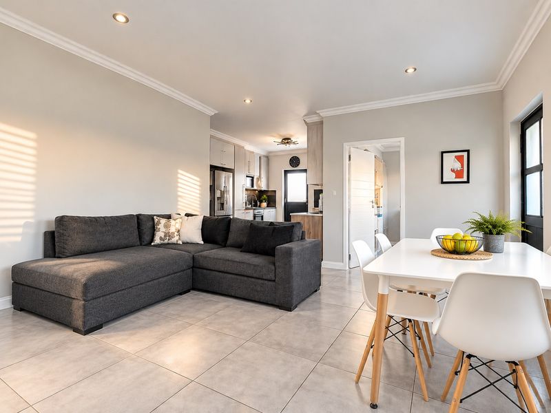 An open-plan living and dining area featuring neutral tiled flooring, recessed lighting, and a modern kitchen with built-in cabinetry and appliances.