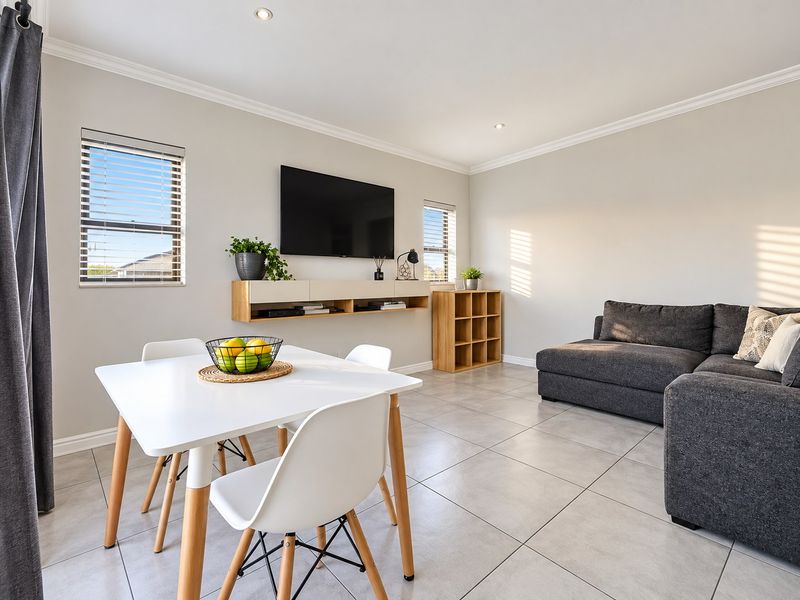 A bright and modern open-plan living and dining area featuring neutral tiled flooring, recessed downlighting, and a sleek floating media console.