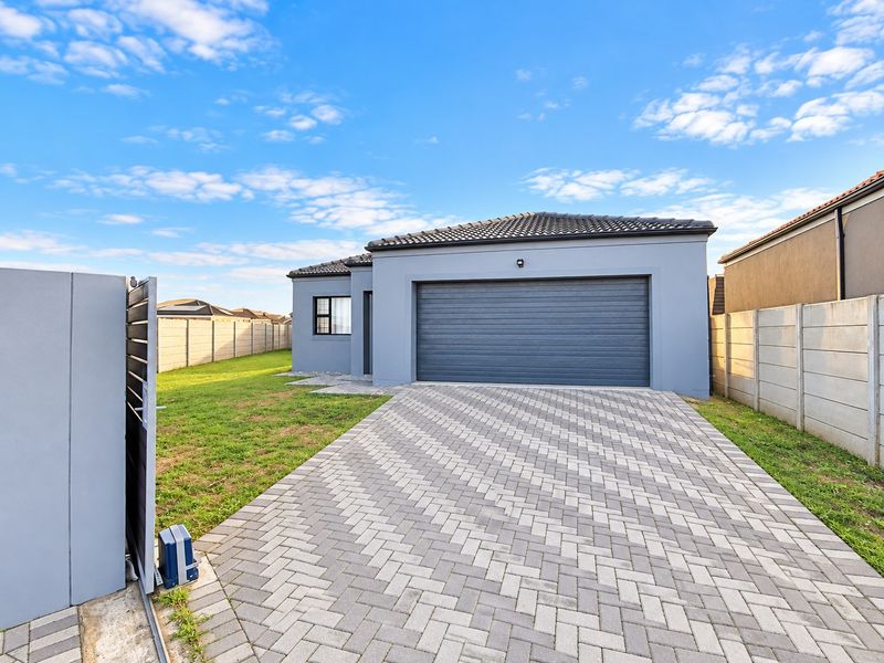 Modern single-story home exterior featuring a paved driveway, automated garage door, and secure perimeter walling in a neat, well-maintained residential setting.